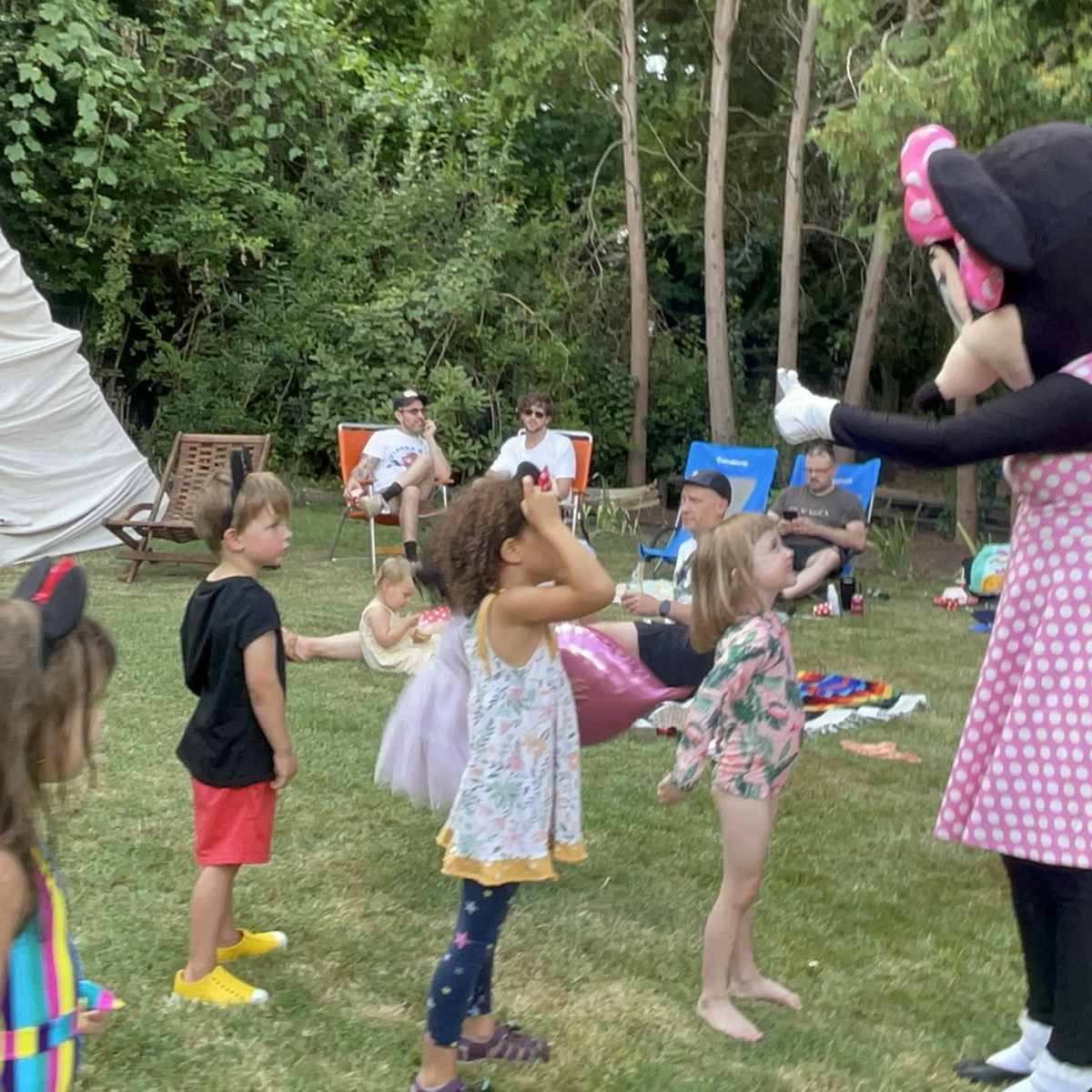 A costumed character resembling a mouse engages with a group of children in a backyard setting.