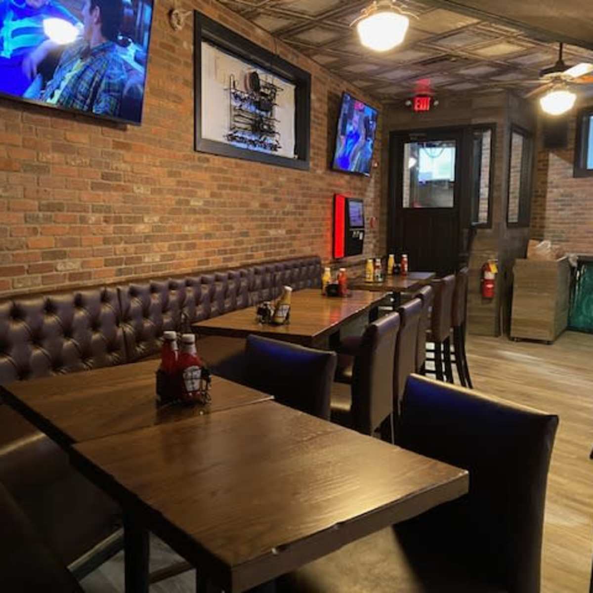A casual dining area with wooden tables, upholstered seating, and multiple televisions mounted on the brick walls.