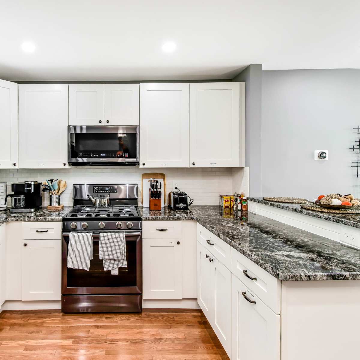 The kitchen features modern white cabinetry, a stainless steel stove, and a granite countertop, with a wooden floor.