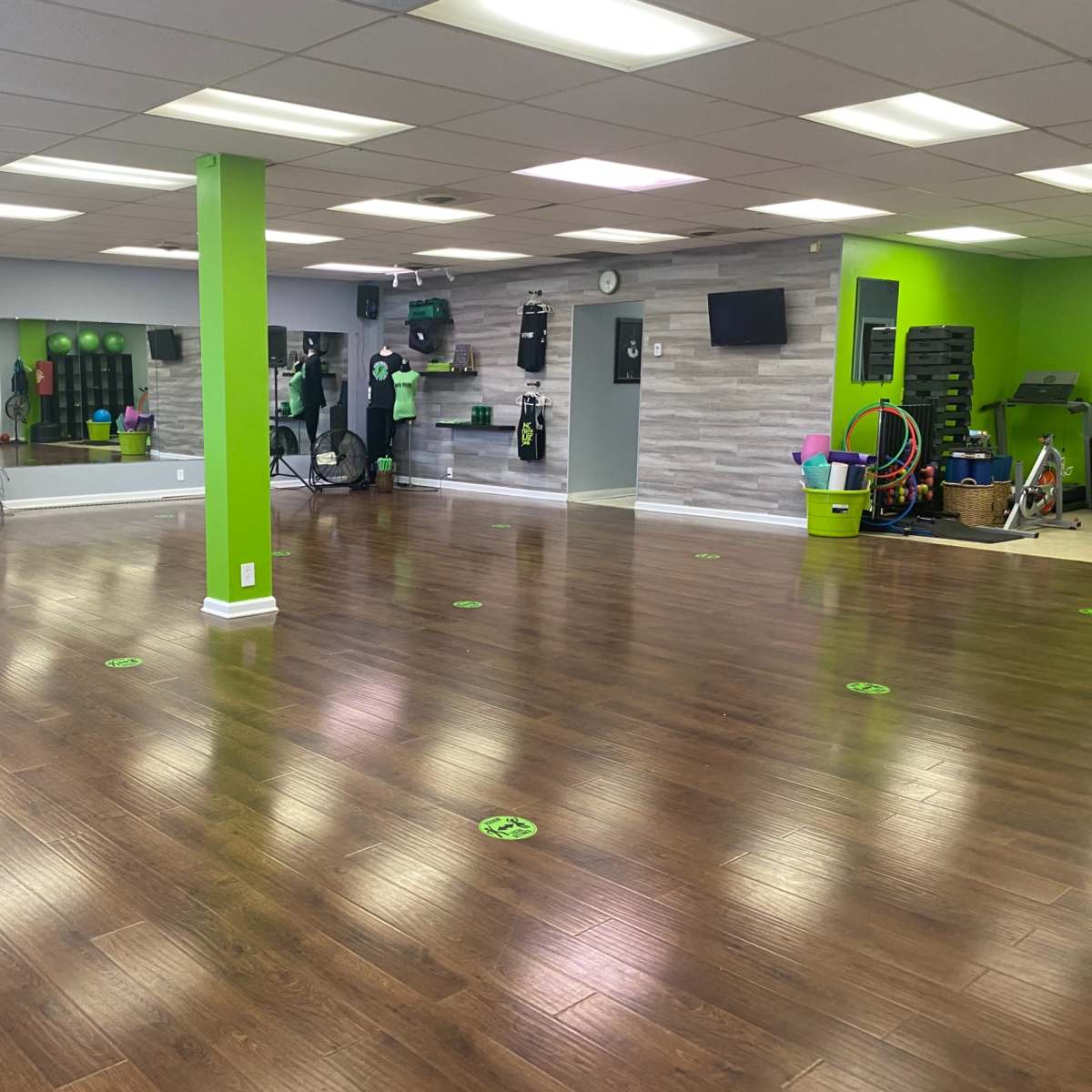 An empty fitness studio with green accent walls, wooden flooring, and various exercise equipment along the walls.