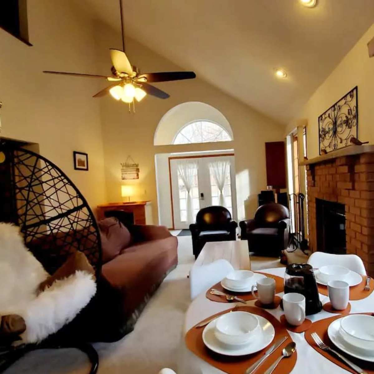 A cozy living room with a hanging chair, a coffee table set for a meal, and large windows allowing natural light to enter.