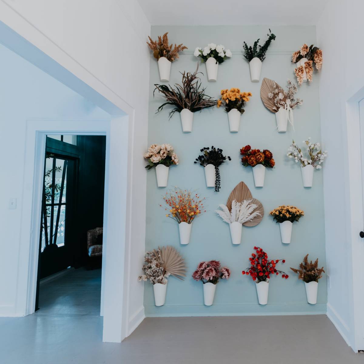 A wall adorned with an arrangement of various dried flowers in wall-mounted white vases.