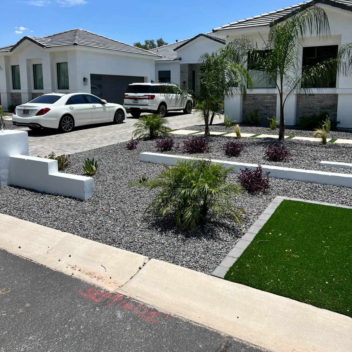 A modern home with a driveway, two parked cars, and a landscaped front yard featuring gravel, plants, and a patch of green grass.