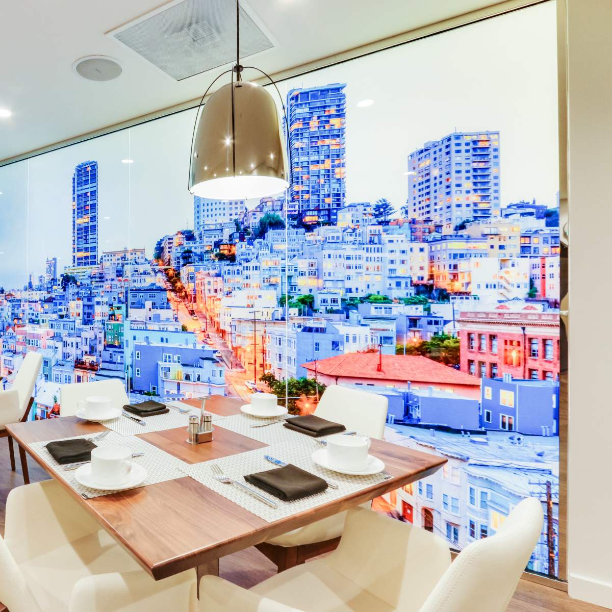 A modern dining area with white chairs and wooden tables, featuring a large wall mural of a cityscape.