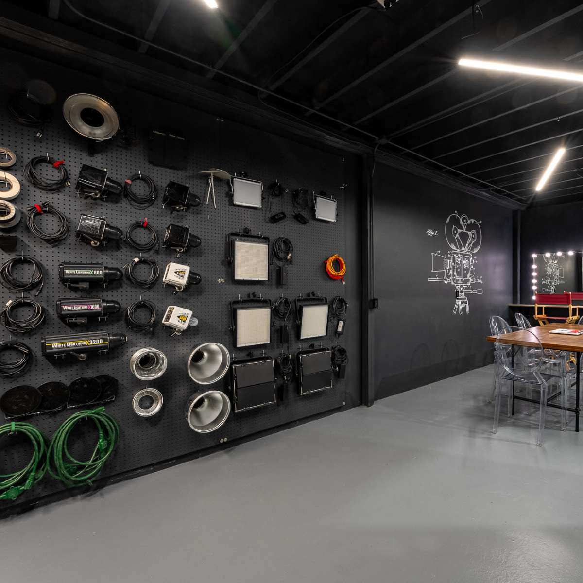A modern interior space featuring a wall with various audio-visual equipment and cables, a table with clear chairs, and a well-lit area with mirrors.