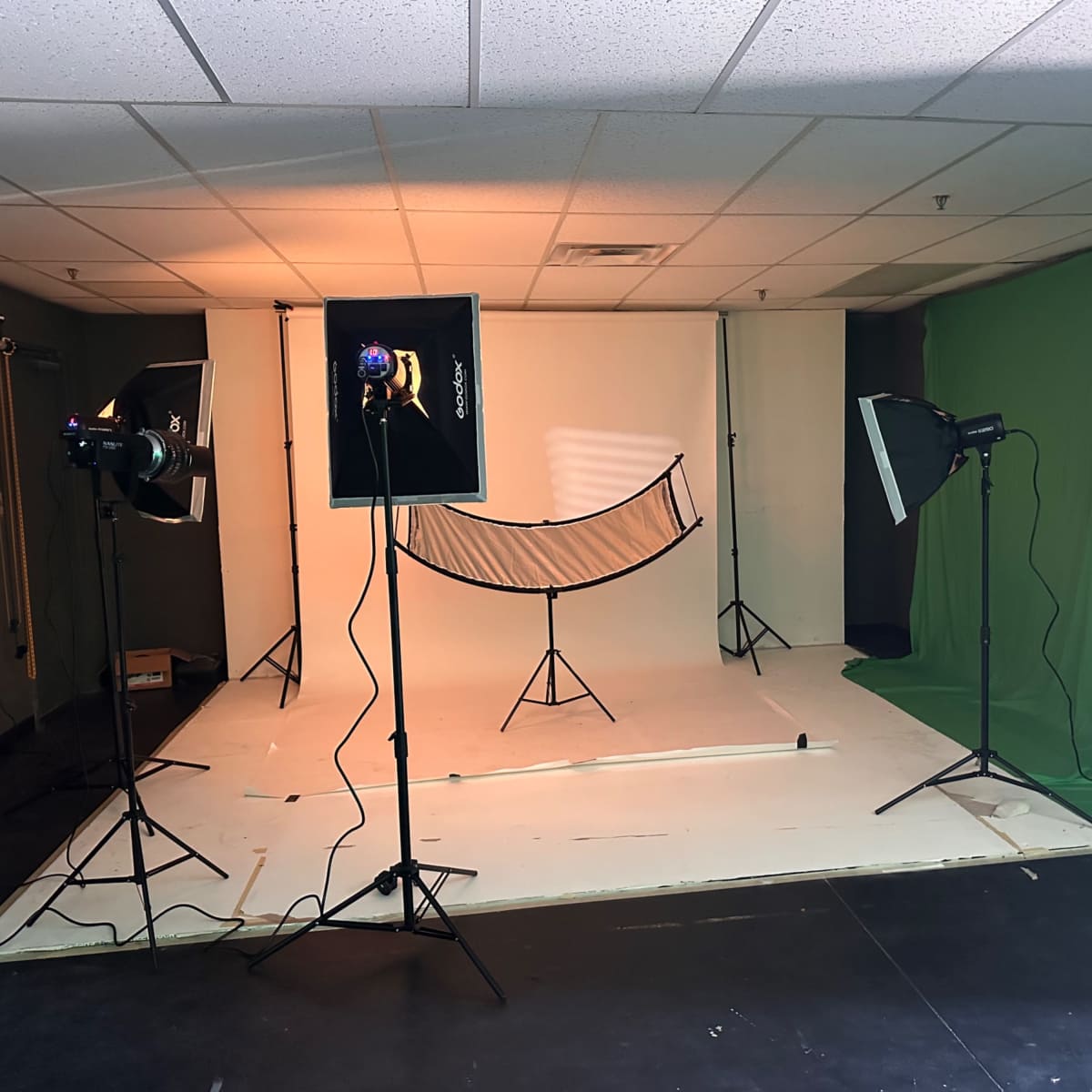 A photography studio setup with a white backdrop, lighting equipment, and a green screen.