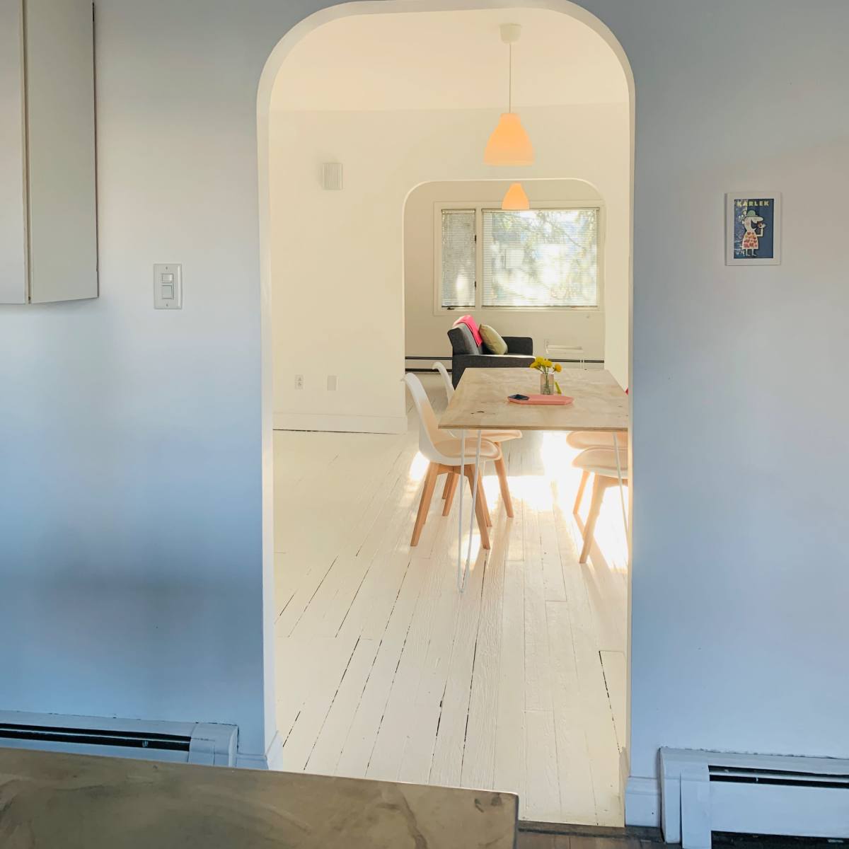 A simple archway leads from a kitchen area into a bright, open living space furnished with a dining table and chairs.