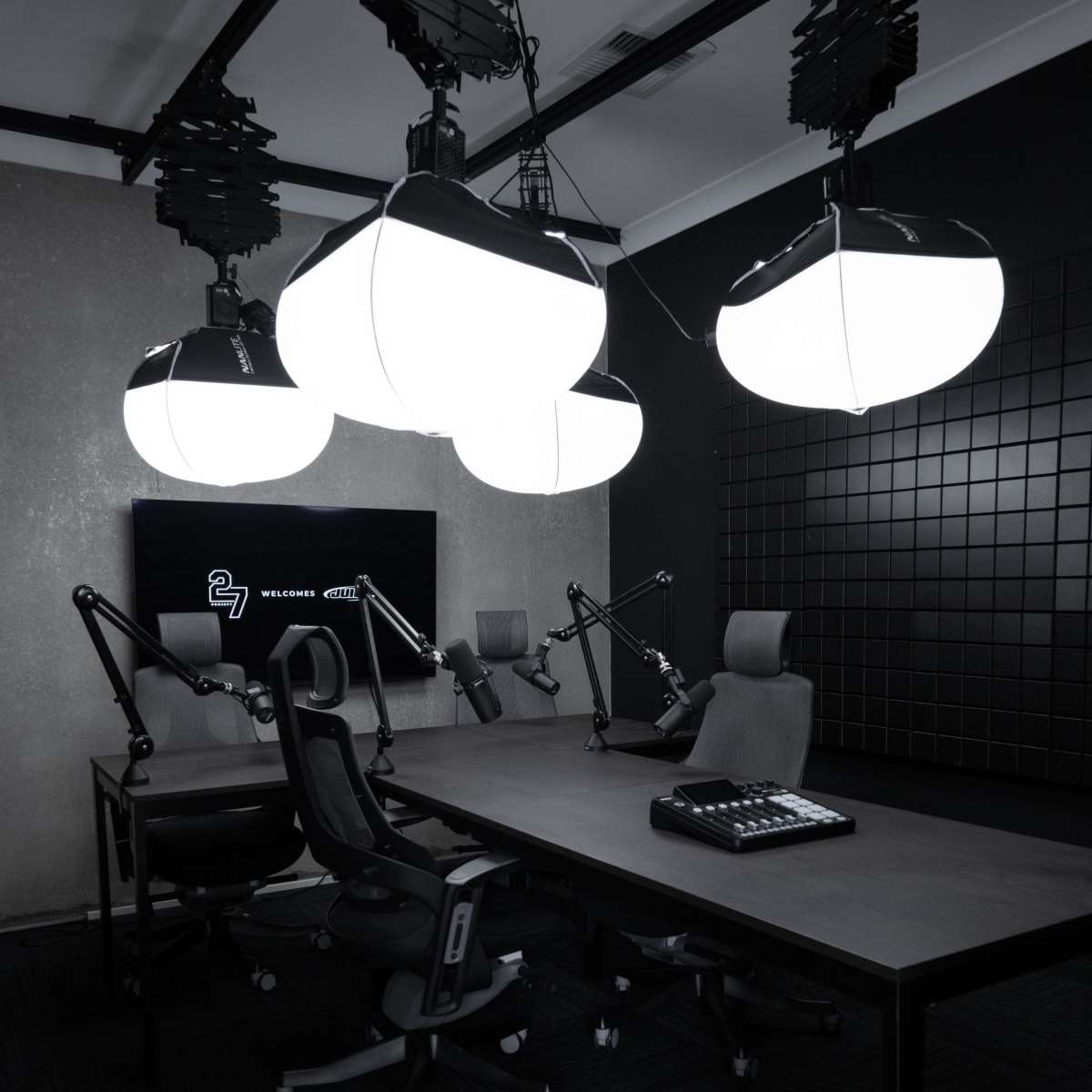 A modern recording studio equipped with a large table, adjustable chairs, and overhead lighting.