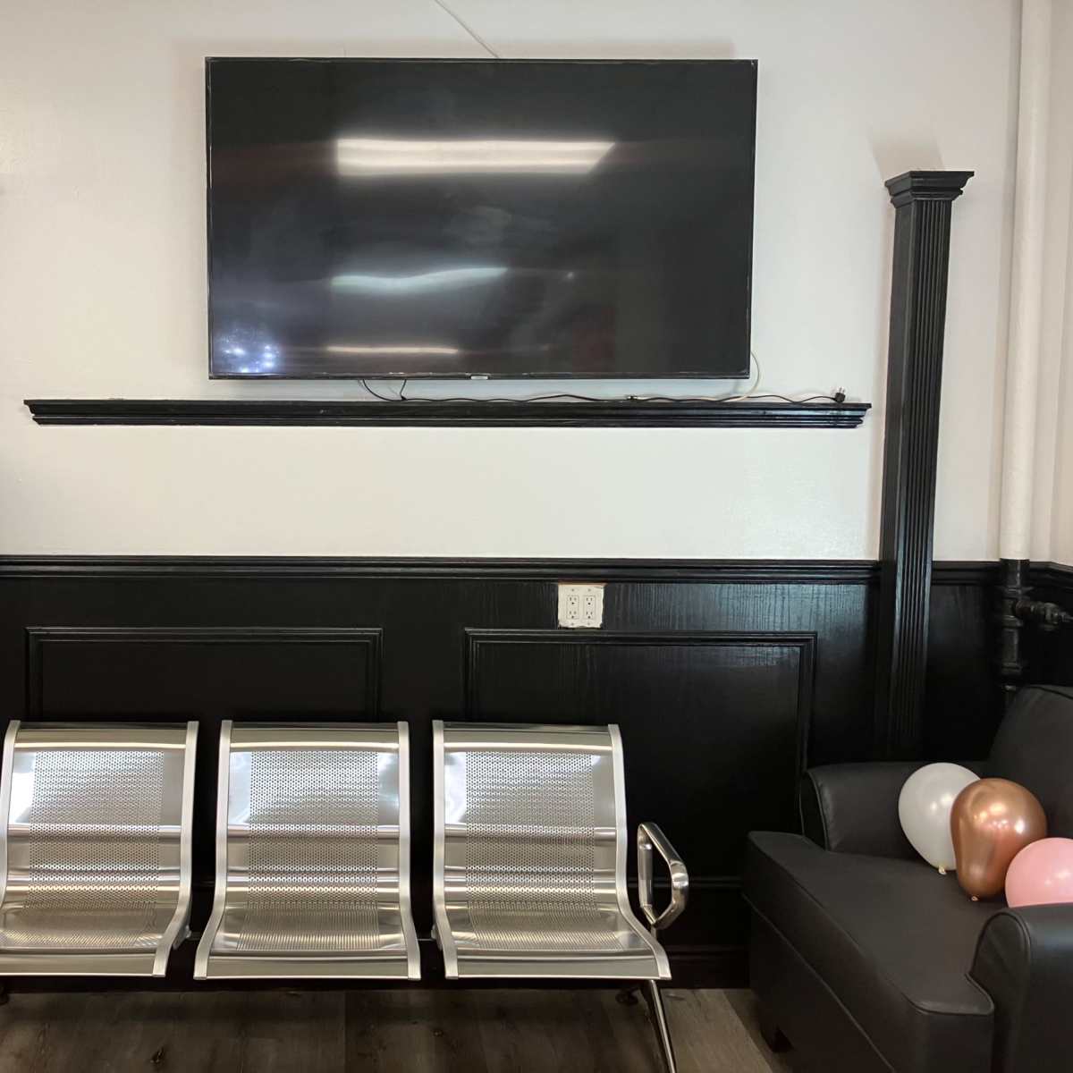 A waiting area with three metal chairs, a television mounted on the wall above, and a speaker beside the seating.