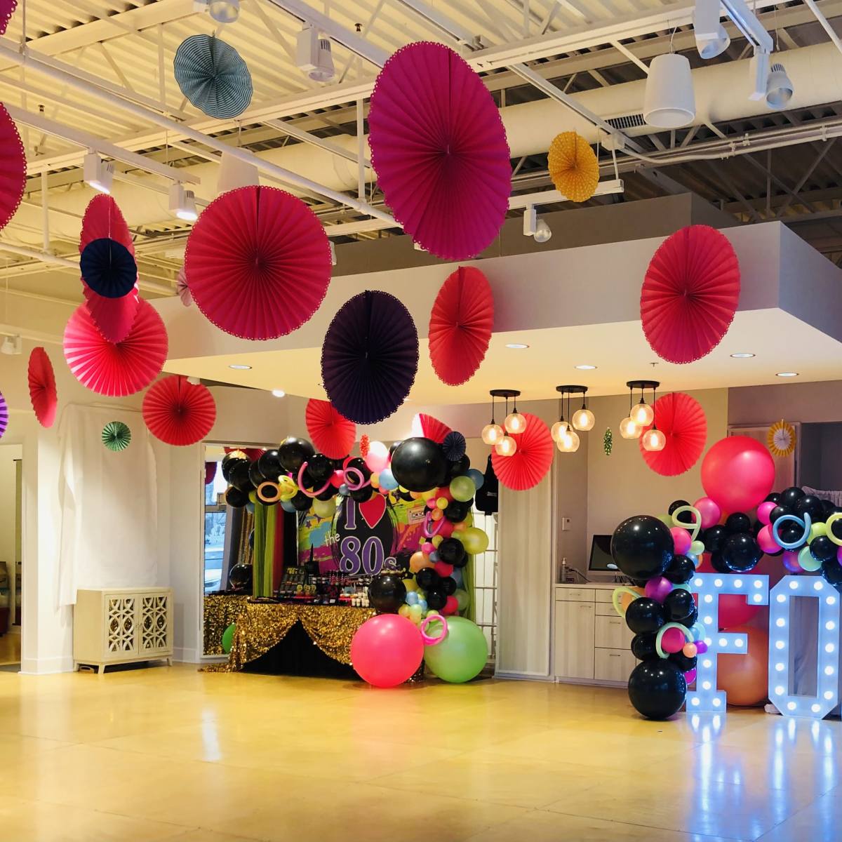 The scene features a decorated event space with colorful paper decorations, large balloons, and a light-up display spelling "FORTY."