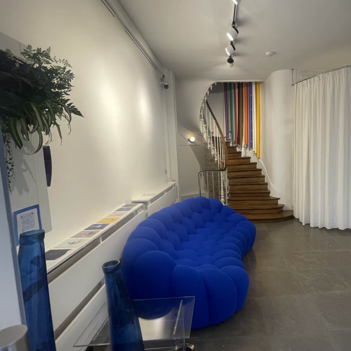 A spacious interior featuring a blue sofa, a staircase with colorful strips, and a curtain separating different areas.