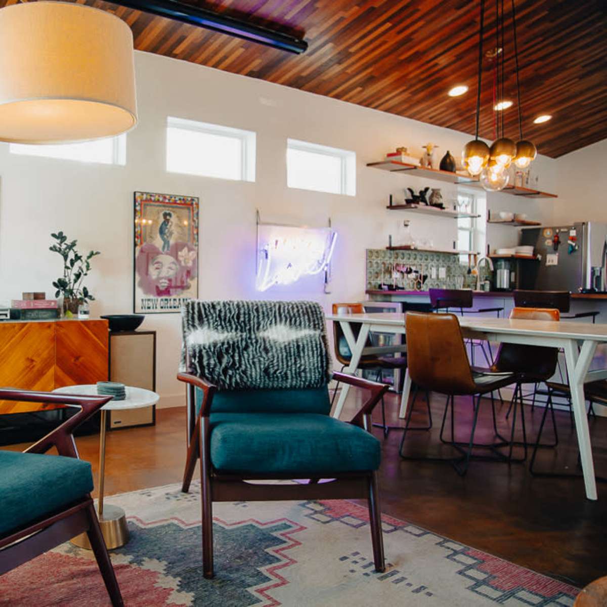A cozy interior space featuring two teal chairs, a floor lamp, and a dining area with a modern kitchen in the background.