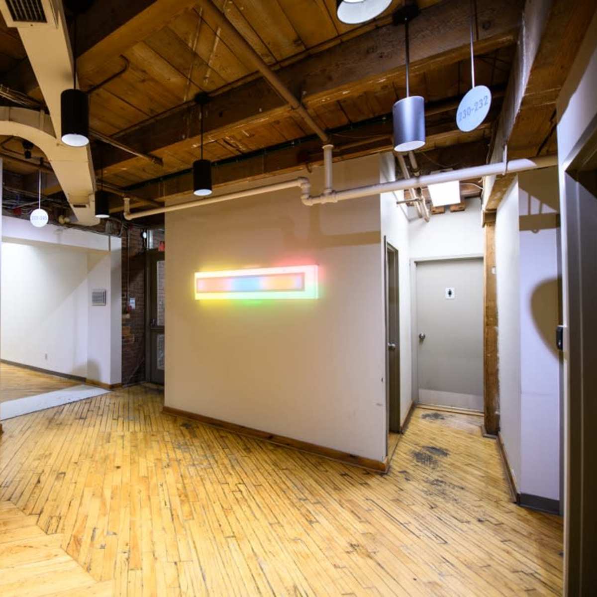 A modern hallway with wooden flooring, featuring doors leading to rooms and a colorful LED light installation on the wall.
