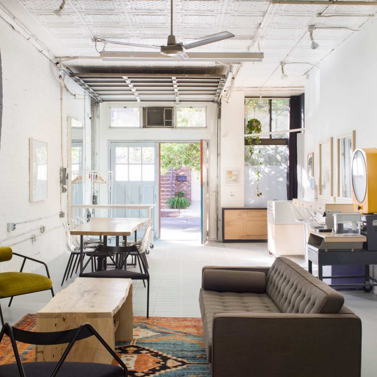 A modern open space with a seating area featuring a couch and chairs, a wooden table, and large windows leading to an outdoor area.