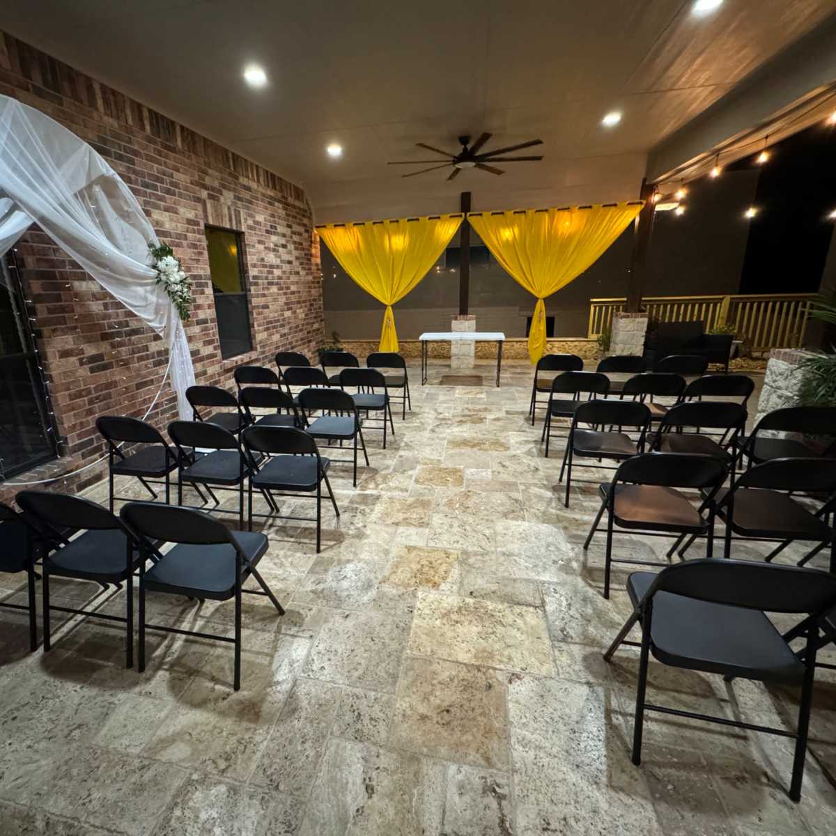 A dimly lit indoor venue with black chairs arranged in rows facing a decorated altar featuring white drapery and yellow curtains.