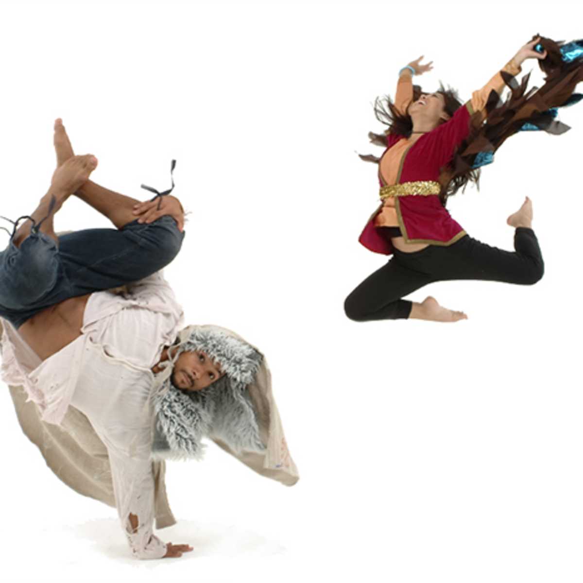 A dancer dressed in a fur-lined hood performs a handstand while another dancer leaps in the air, both set against a white background.