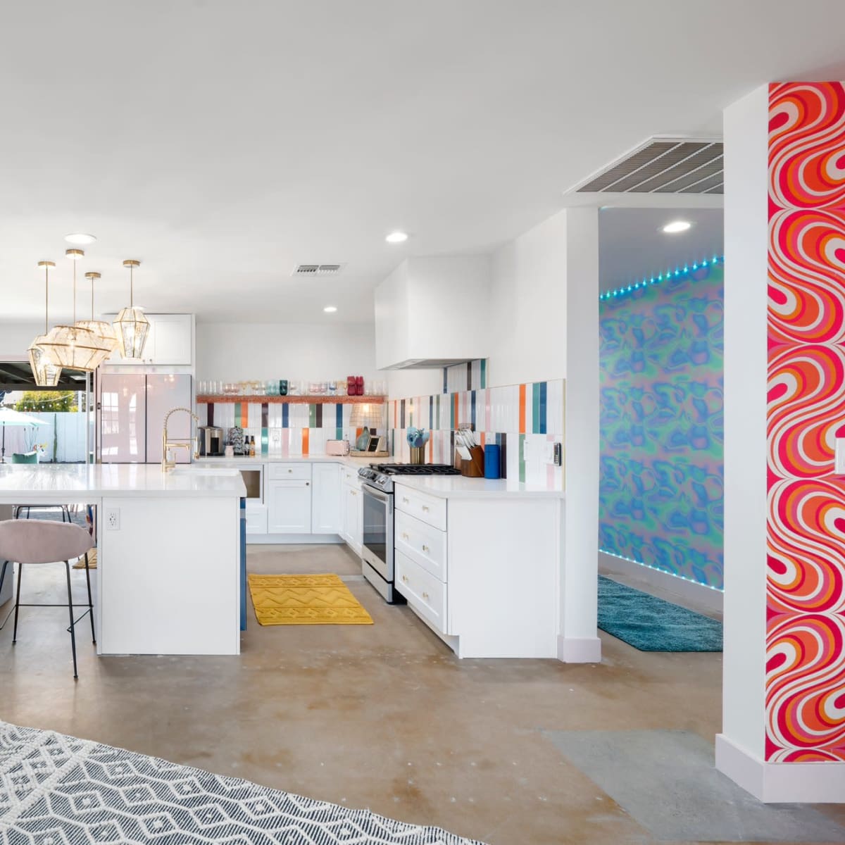 A modern kitchen features white cabinetry, colorful tile accents, and a dining area with pink bar stools.