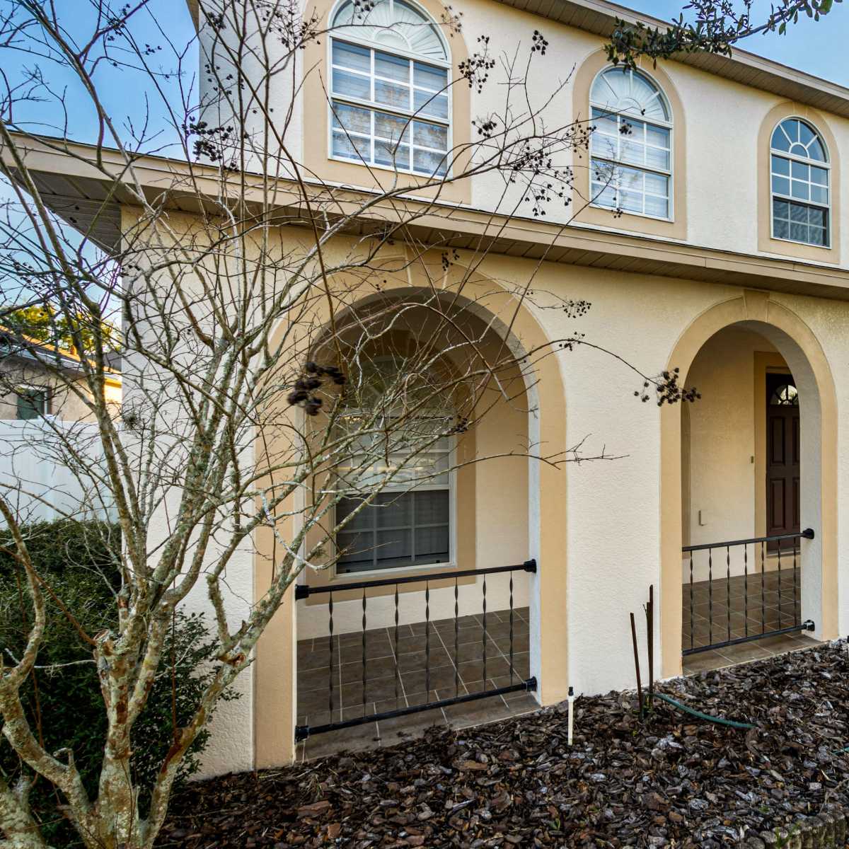 A two-story house with arched entryways, multiple windows, and a driveway leading to a garage on the side.