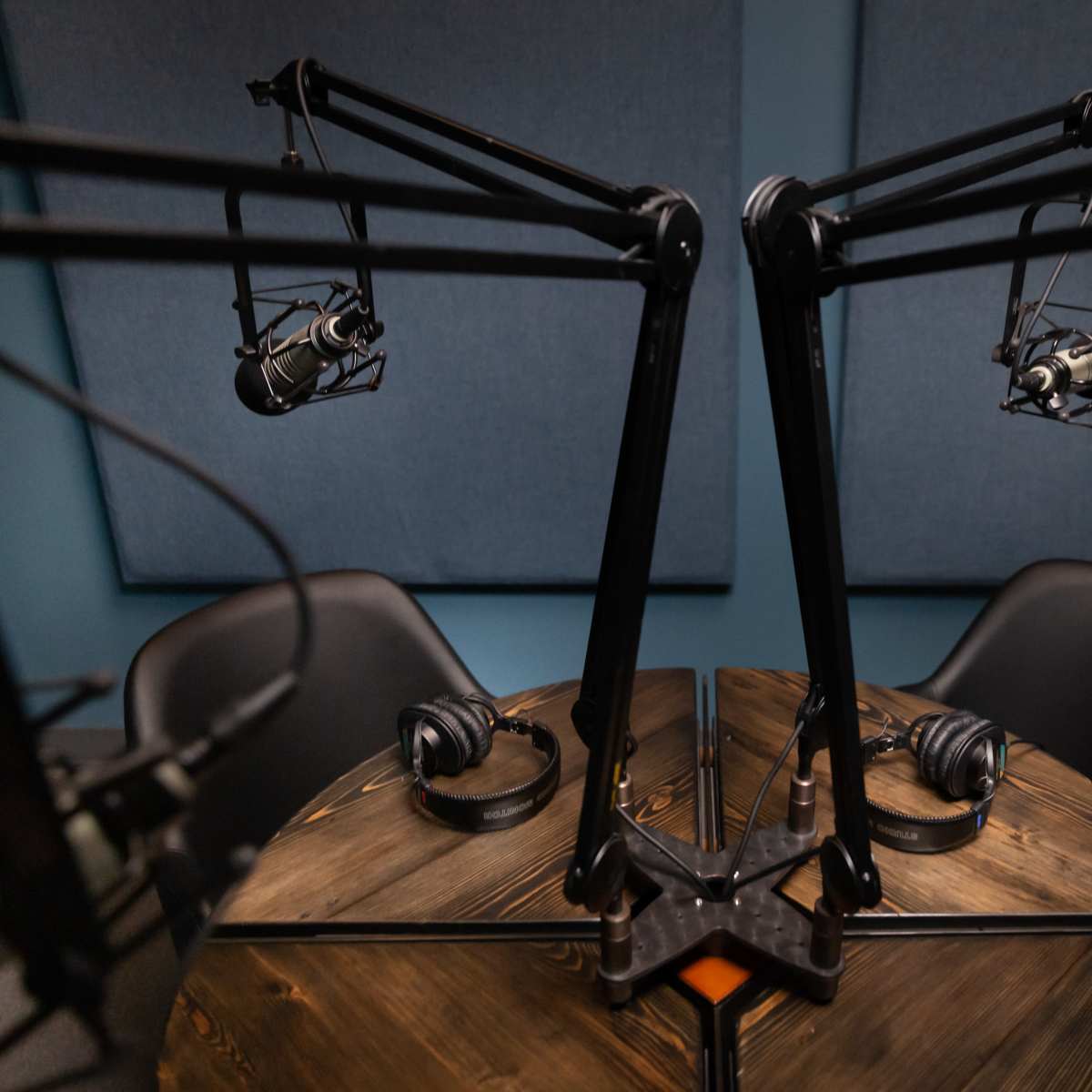 A podcast recording studio featuring two microphone setups on adjustable stands facing a round wooden table with headphones placed on it.