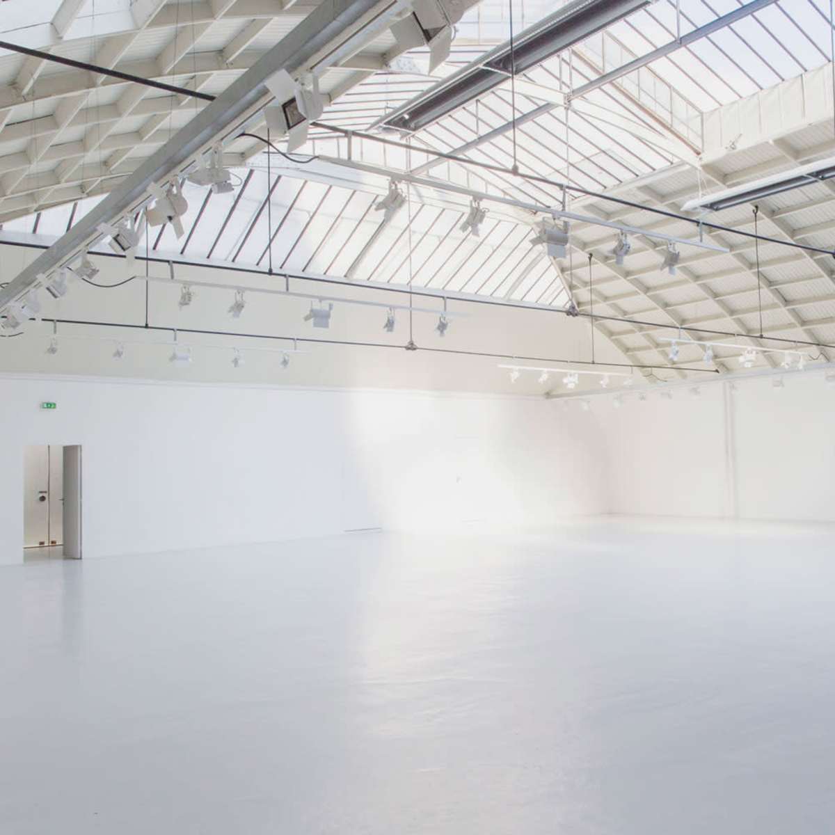 A spacious, well-lit art gallery with a high ceiling and a staircase in one corner.