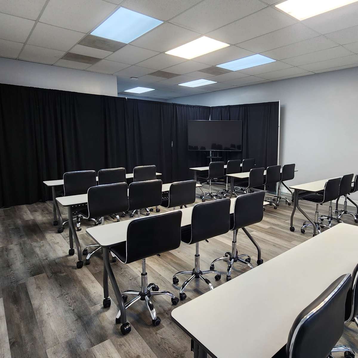 A classroom with rows of desks and chairs arranged facing a large screen, separated by black curtains at the back.