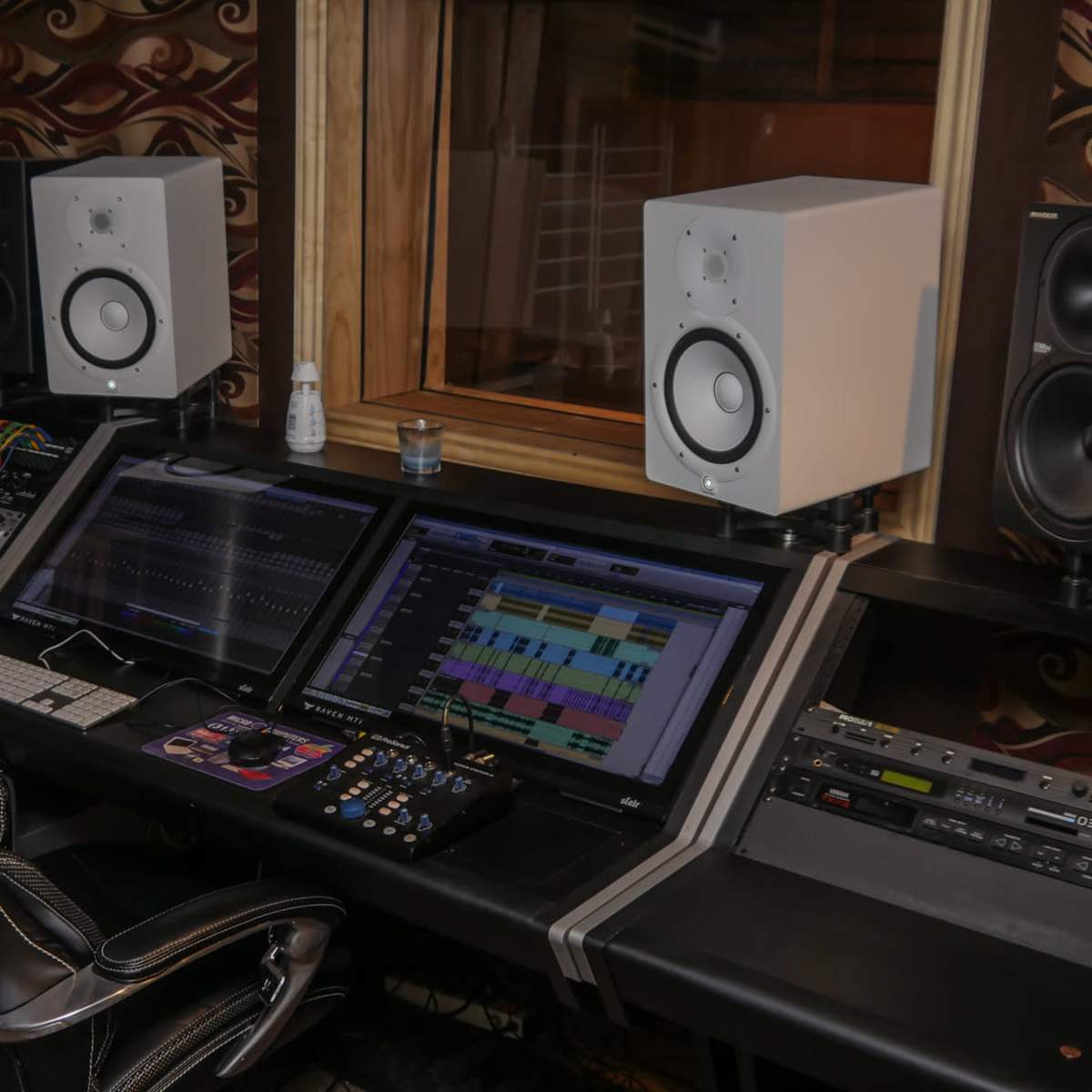 A sound mixing studio featuring dual computer monitors, studio monitors, and various audio equipment arranged on a sleek desk.