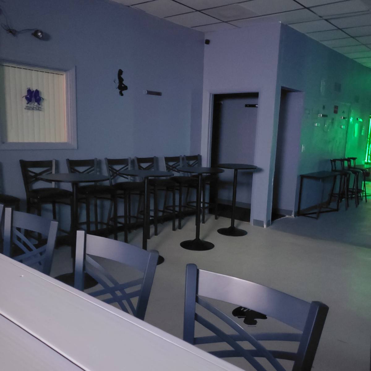 A sparsely furnished bar area with several high tables and chairs against a purple wall.