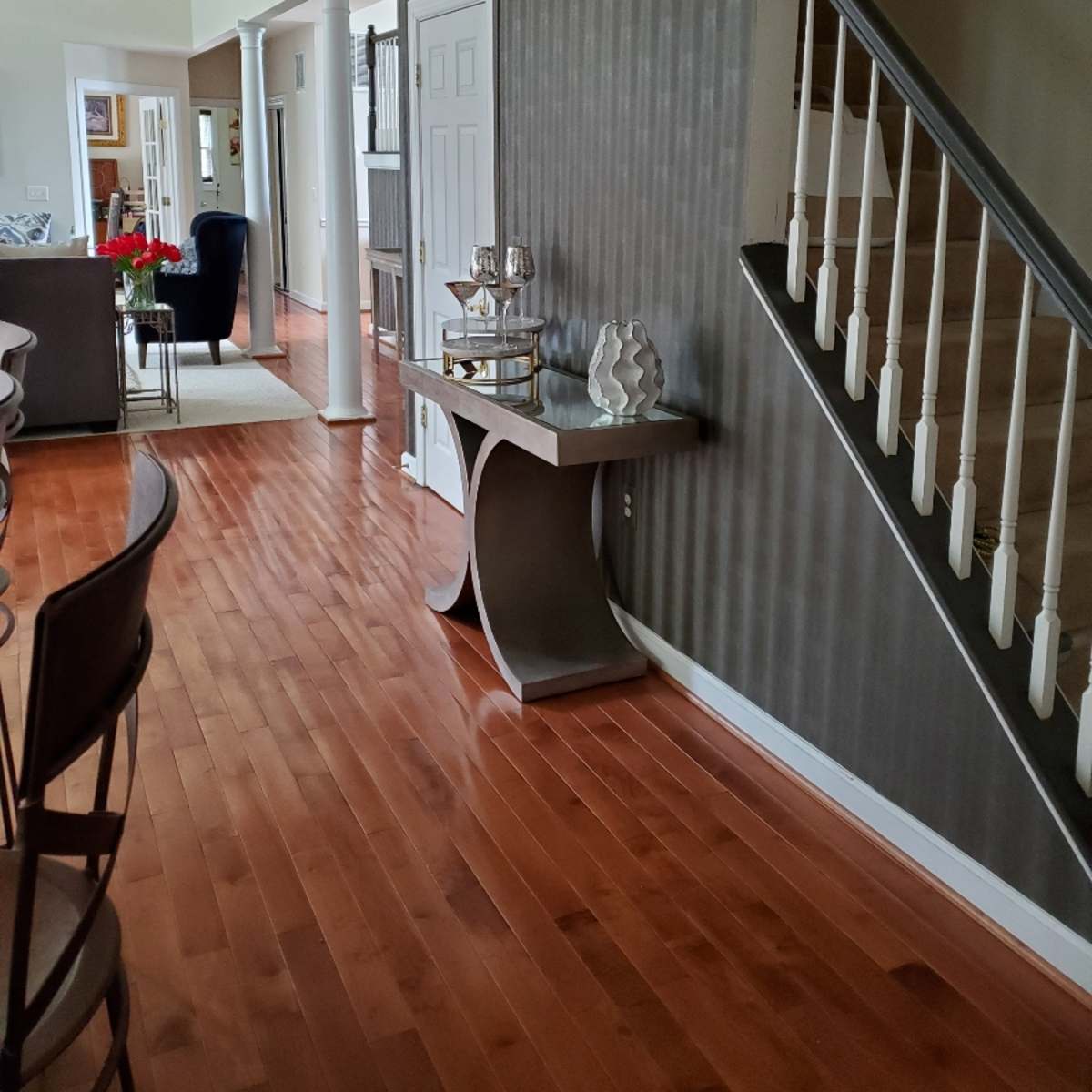 A hallway with hardwood floors, a decorative table against a striped wall, and a staircase leading to an upper level.