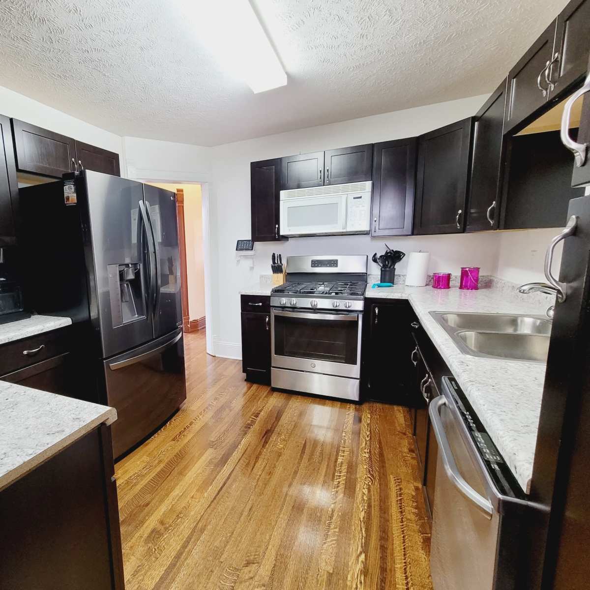 A modern kitchen features dark cabinetry, stainless steel appliances, and granite countertops with hardwood flooring.