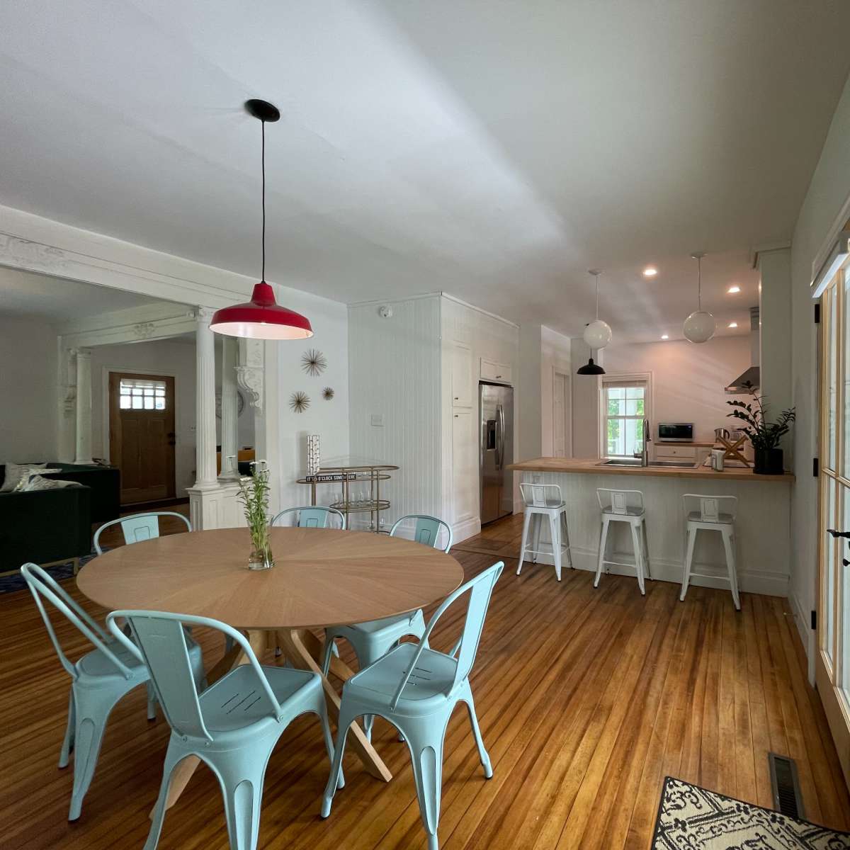 A dining area features a round wooden table surrounded by light blue chairs, with an open kitchen visible in the background.