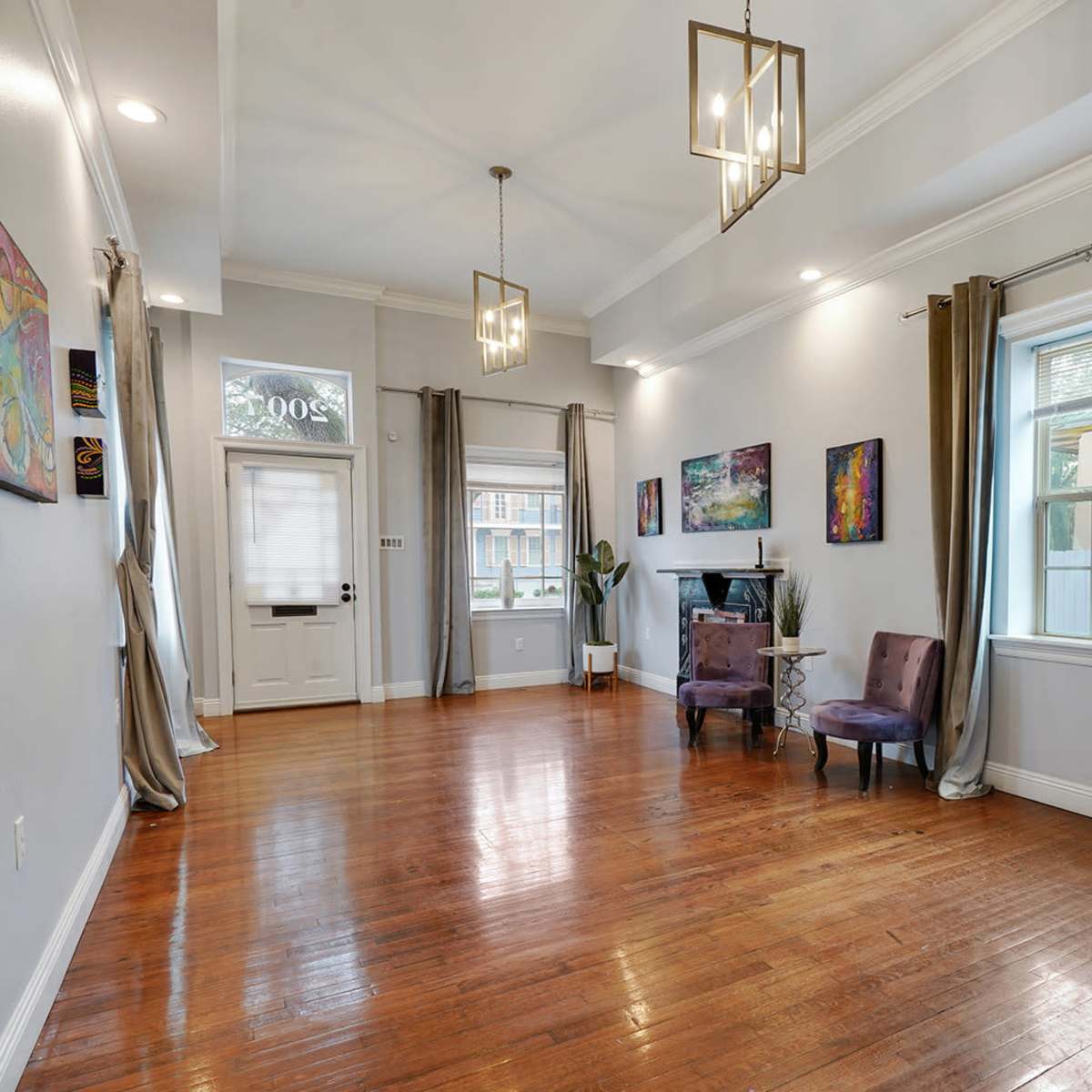 A spacious interior room features wooden flooring, light-colored walls, decorative artwork, and two chairs near a window.