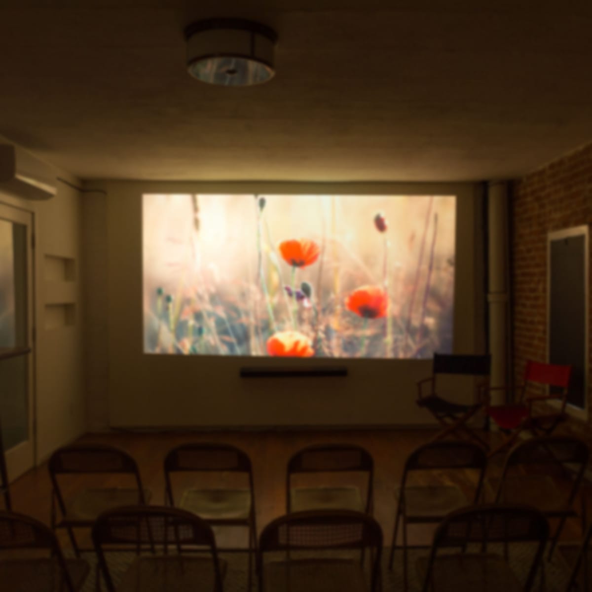 A room with a large screen displaying a floral image and several rows of chairs arranged in front of it.