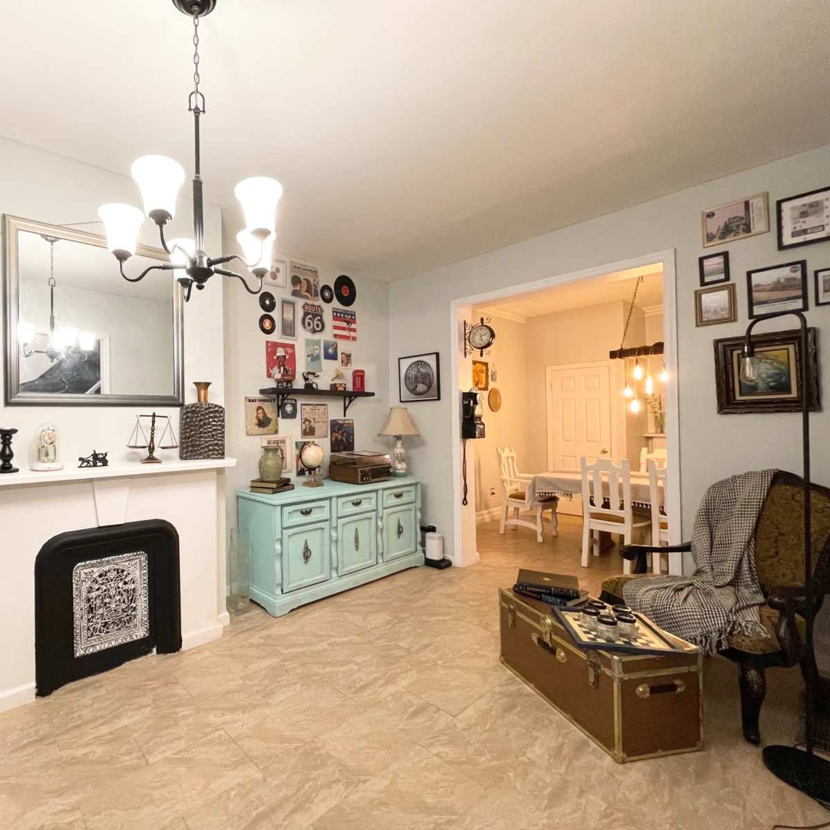A living room with a fireplace, a turquoise sideboard, vintage decorations on the walls, and a dining area visible through an archway.