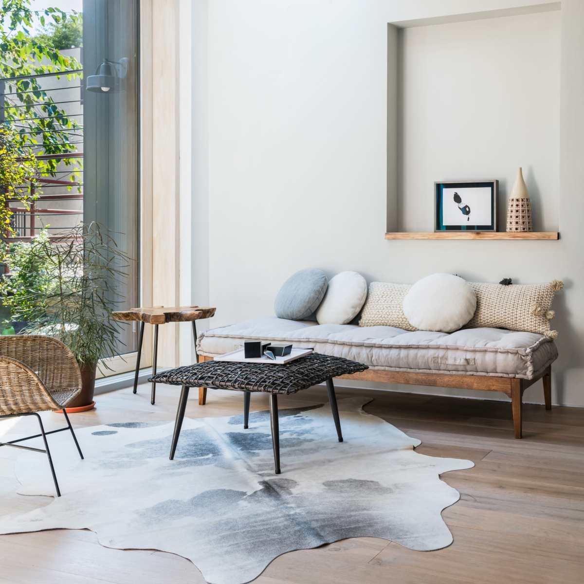 A modern living room with a daybed, a low coffee table, a patterned rug, and large windows allowing natural light to illuminate the space.