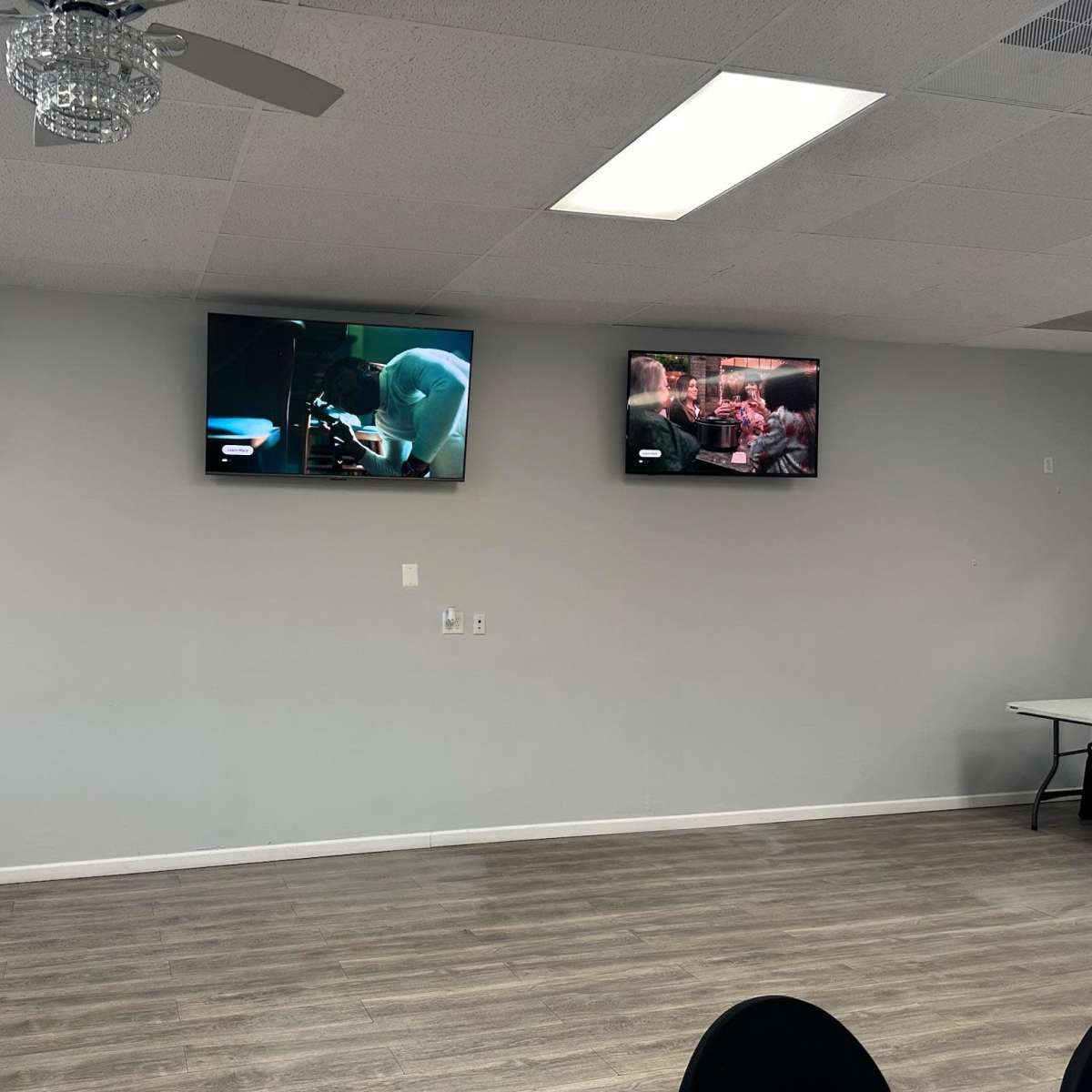 Three television screens are mounted on a light gray wall, each displaying different scenes from various shows or movies.