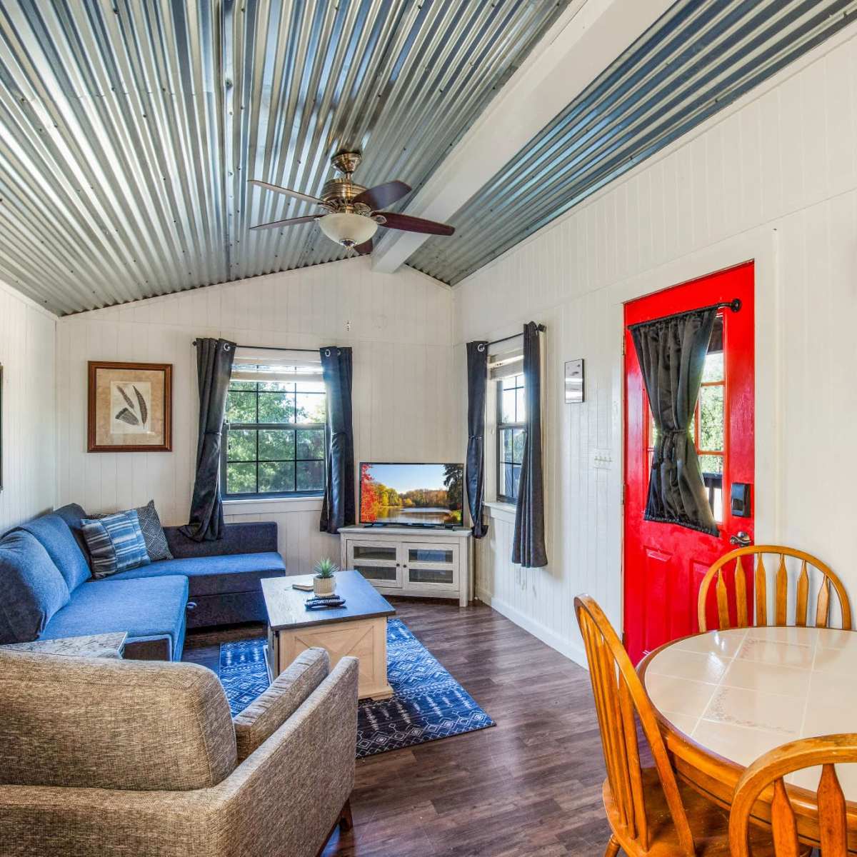 A small living area features a gray sofa, a round dining table, and a bright red front door.