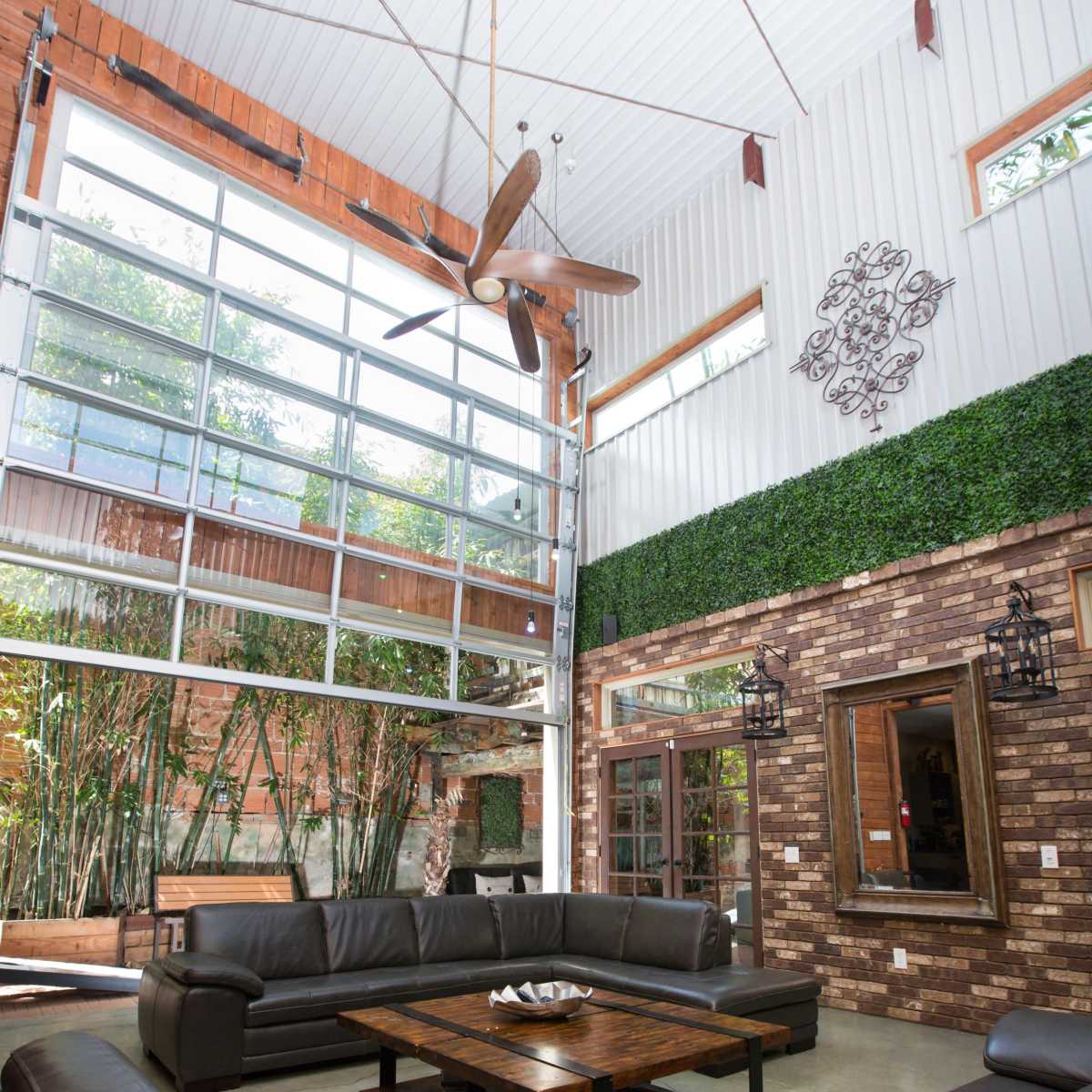 A spacious living room with a high ceiling, large windows, and modern furnishings arranged around a central coffee table.