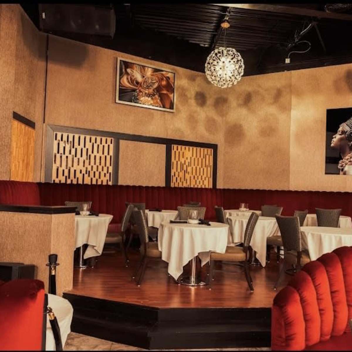 A stylish restaurant interior featuring round tables covered with white tablecloths, red upholstered seating, and decorative artwork on the walls.
