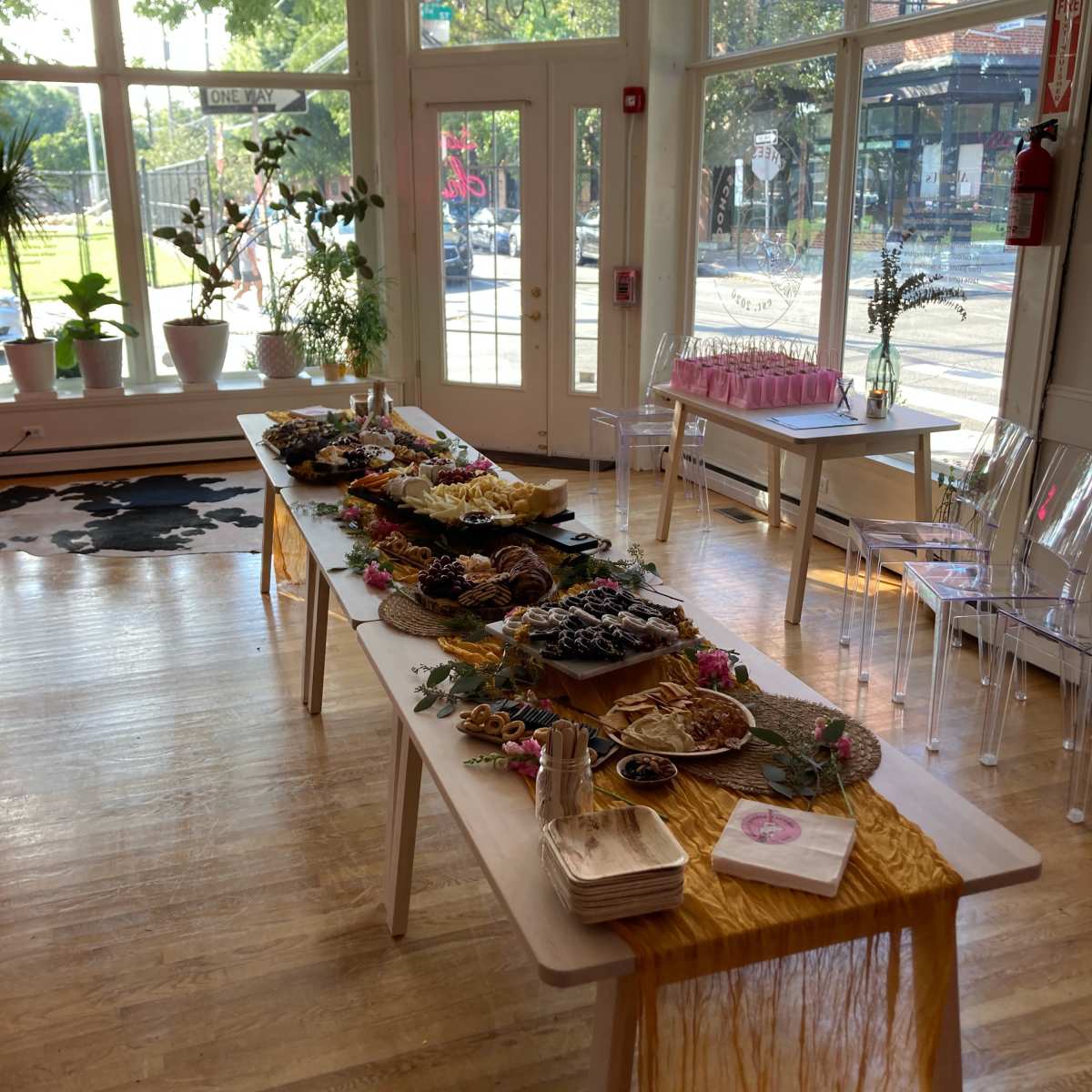 A large, elegantly set table featuring a variety of food platters is displayed in a bright, airy room with large windows.