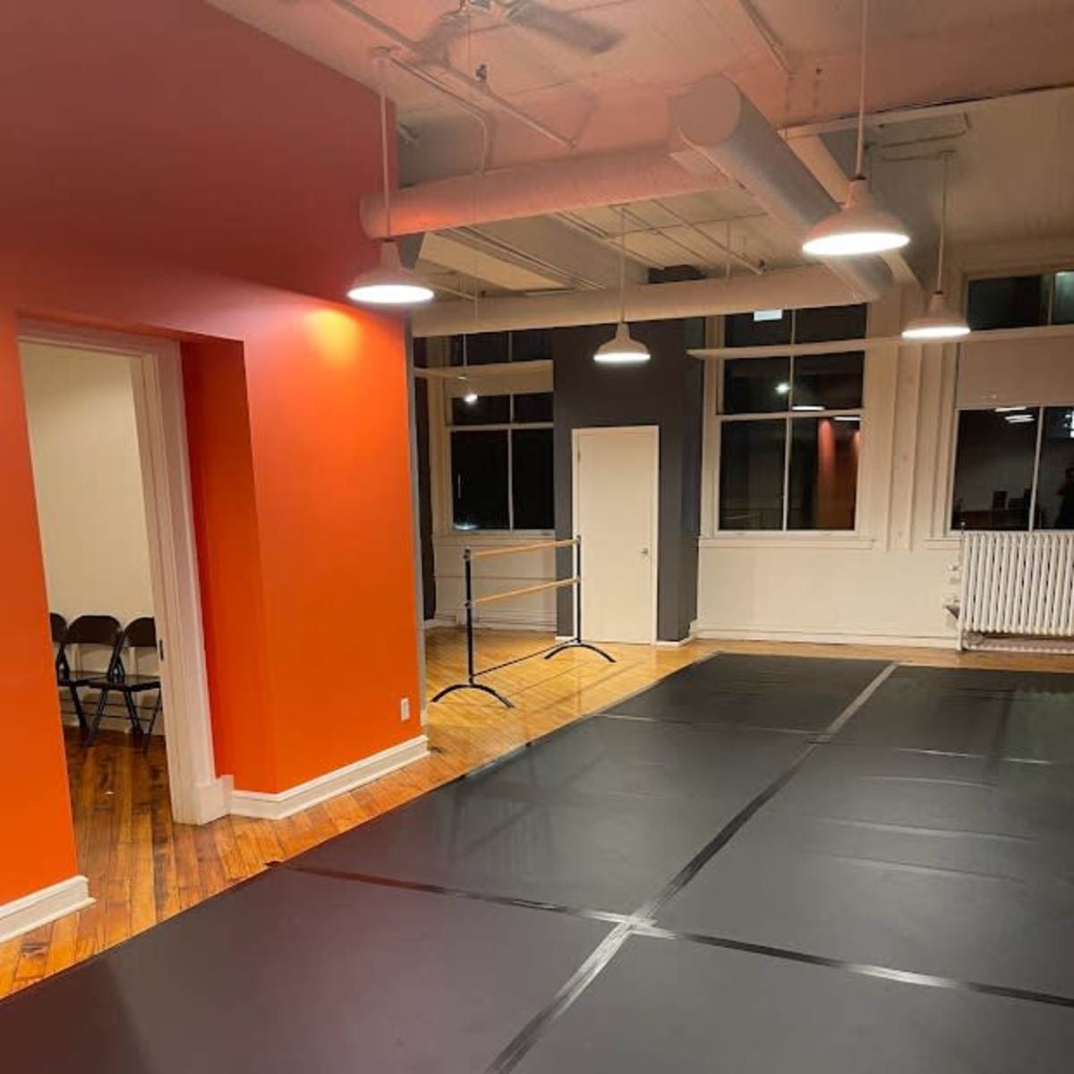 A spacious room with black mats on the floor, orange walls, and large windows illuminated by pendant lights.