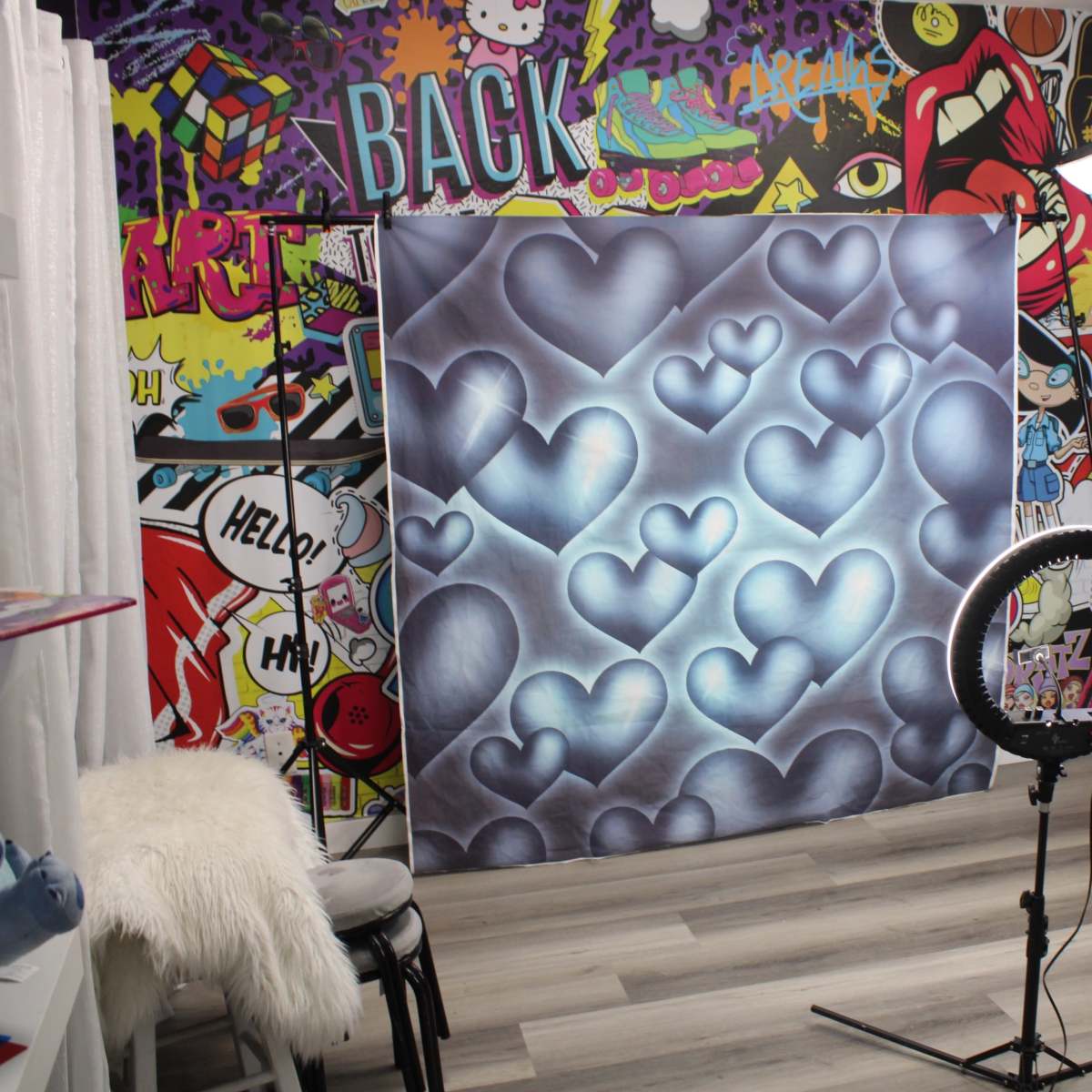 A photography studio with a heart-patterned backdrop, a ring light, and colorful graffiti-style wall art.
