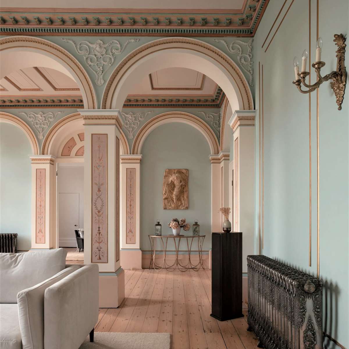 A spacious interior featuring arched doorways, a light blue wall with decorative trim, and a mix of modern and classical furnishings.