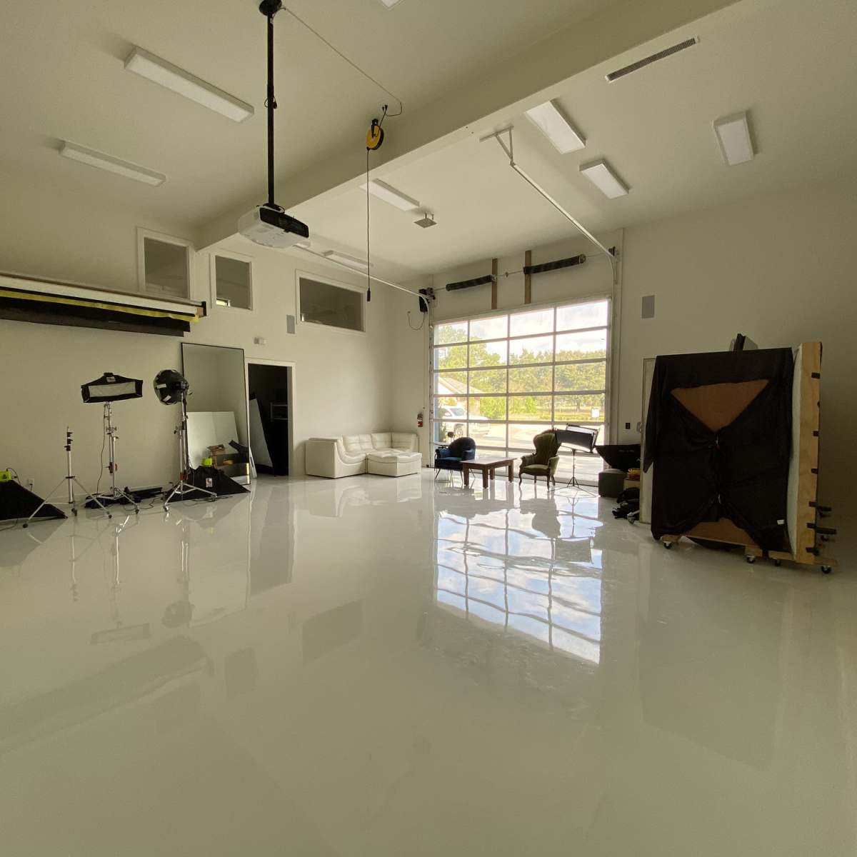 A spacious, well-lit studio with white walls, a shiny floor, and various photography equipment arranged in the room.