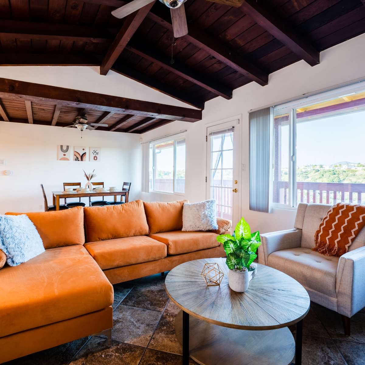 A cozy living room featuring an orange sectional sofa, a round coffee table, and large windows with views of the outdoors.