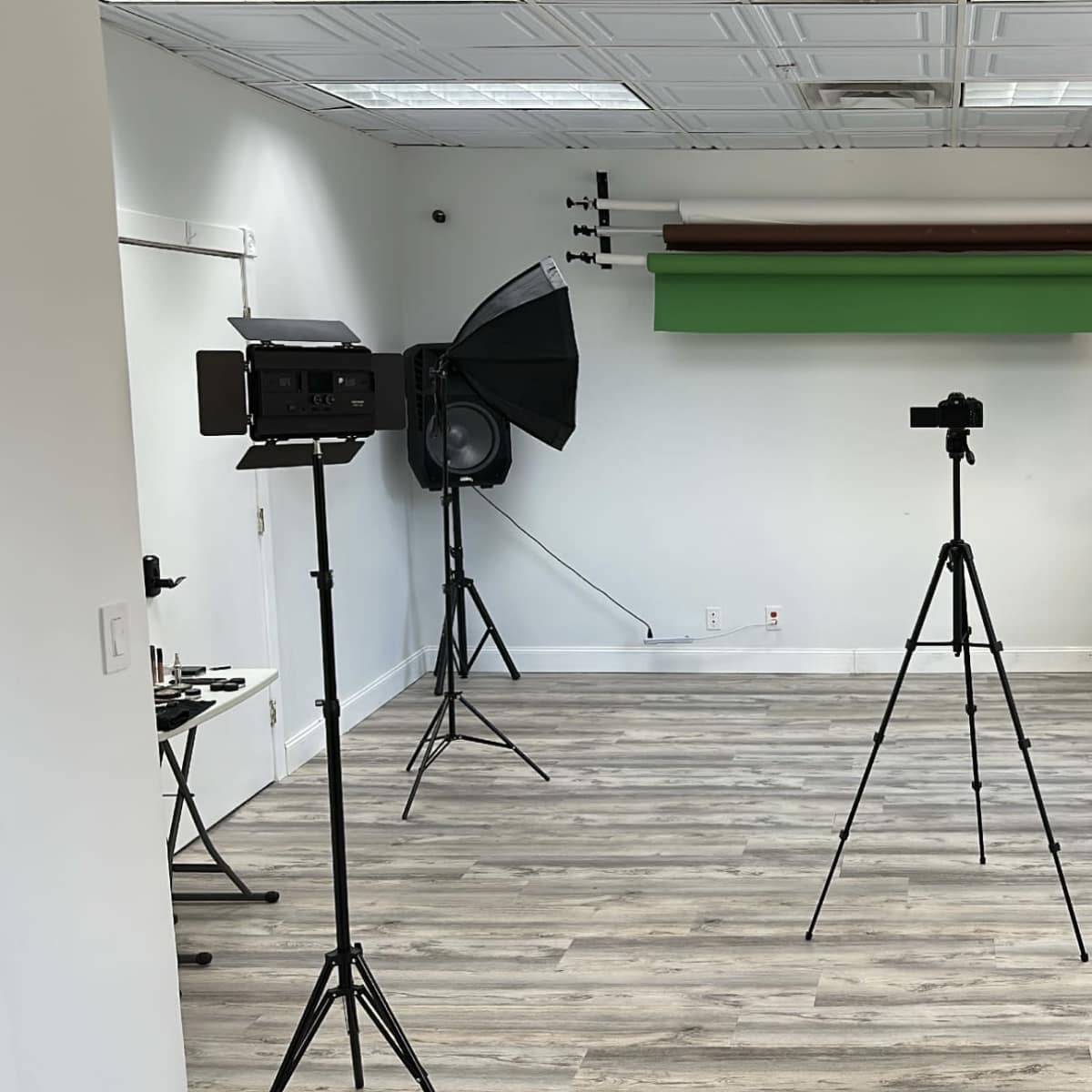 A photography studio featuring three tripods with cameras, two softbox lights, and a green backdrop.