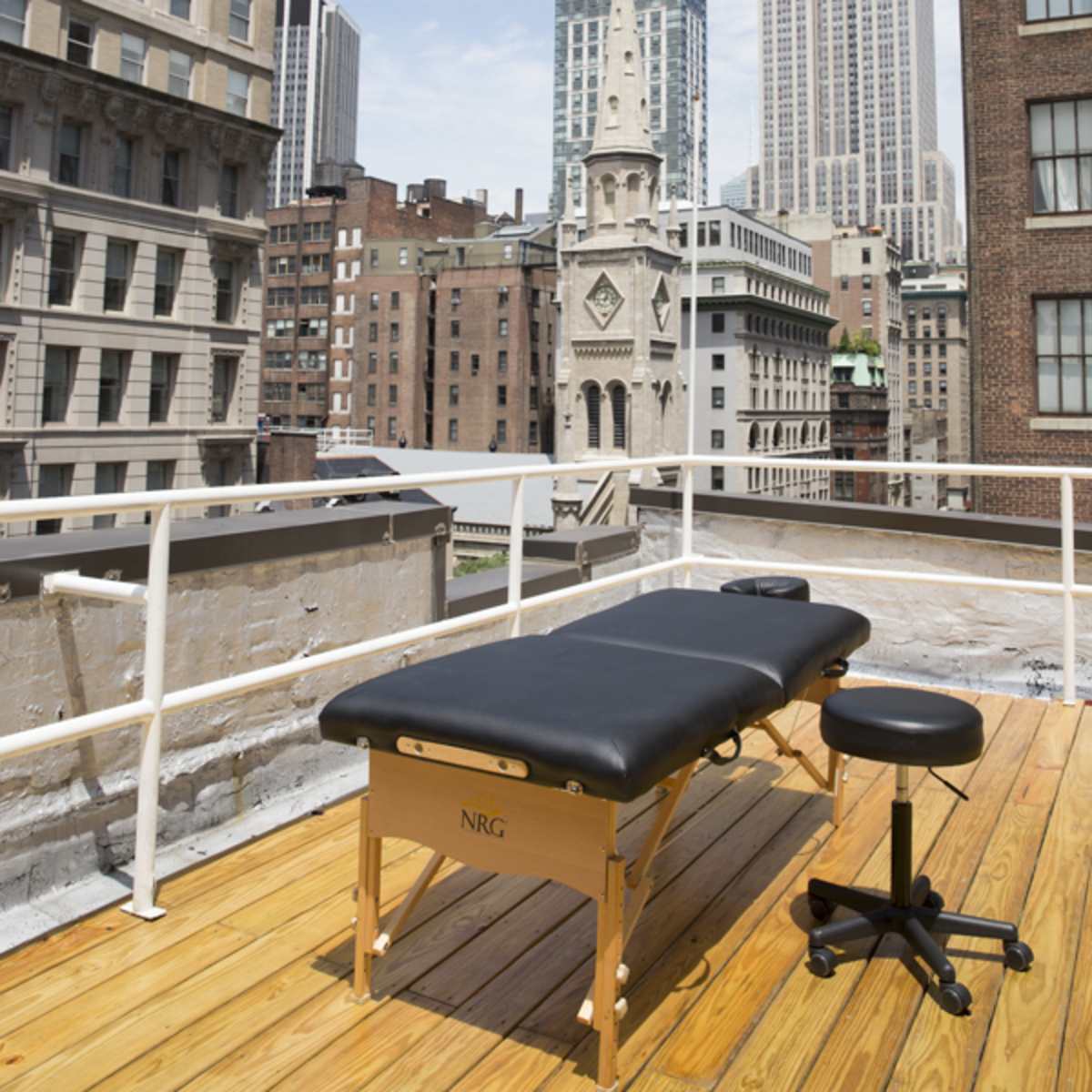 A massage table and stool are positioned on a rooftop deck with the Empire State Building visible in the background.