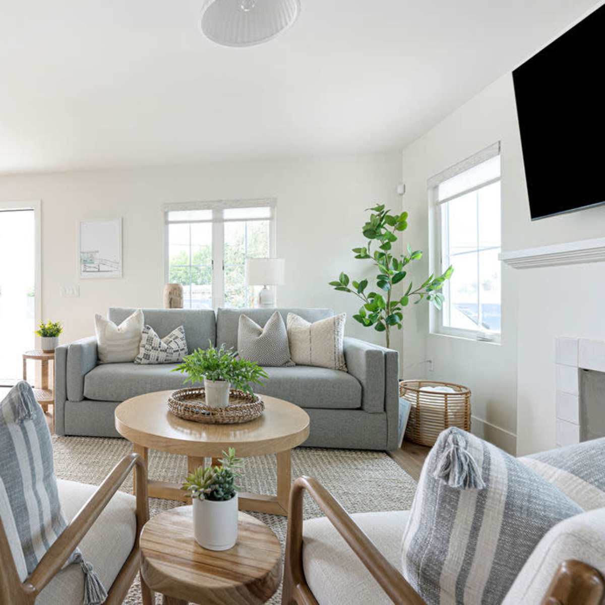 A bright living room with a gray sofa, two armchairs, a round coffee table, and large windows letting in natural light.