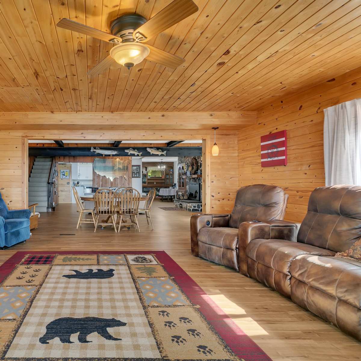 A cozy wooden living space featuring a patterned area rug with bear designs, comfortable seating, and a ceiling fan.