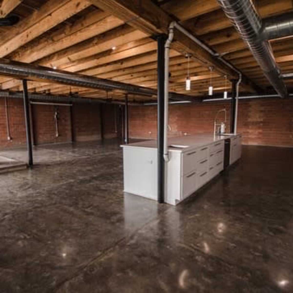 A spacious, unfinished kitchen area with exposed beams and concrete flooring.