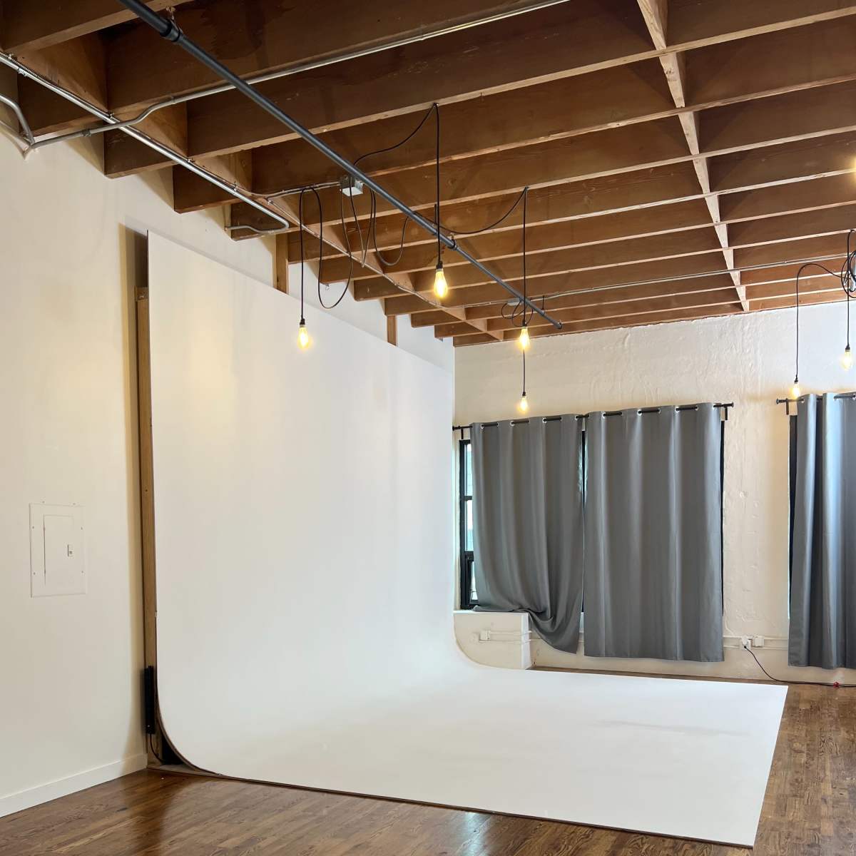 A spacious photography studio with a seamless white backdrop, wooden floors, and gray curtains.